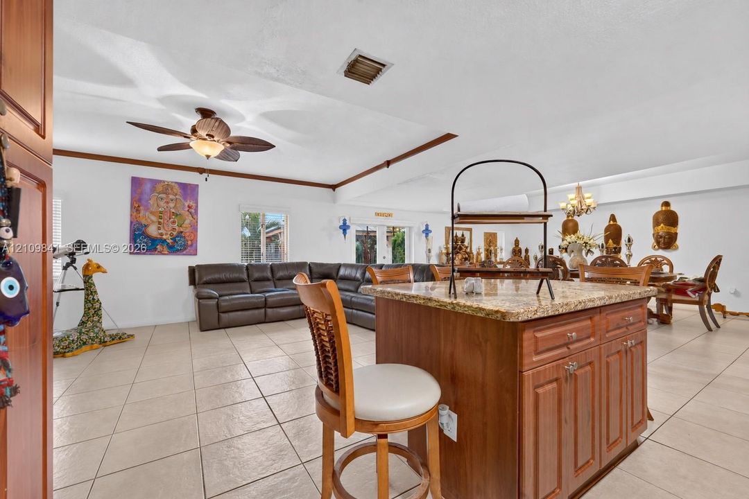 Kitchen featuring a central island with natural stone countertop, wood cabinetry, tile flooring, and a ceiling-mounted fan