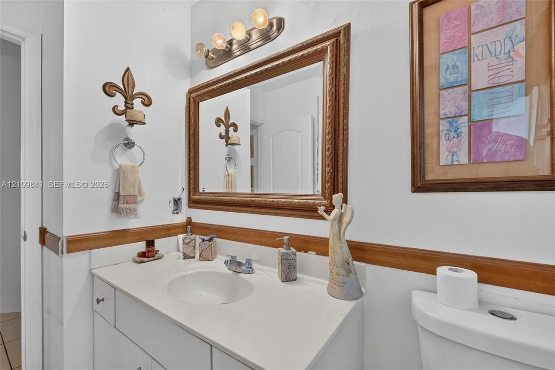 Vanity with an integrated sink, wooden chair rail, wall-mounted mirror with a metallic frame, and four-bulb light fixture