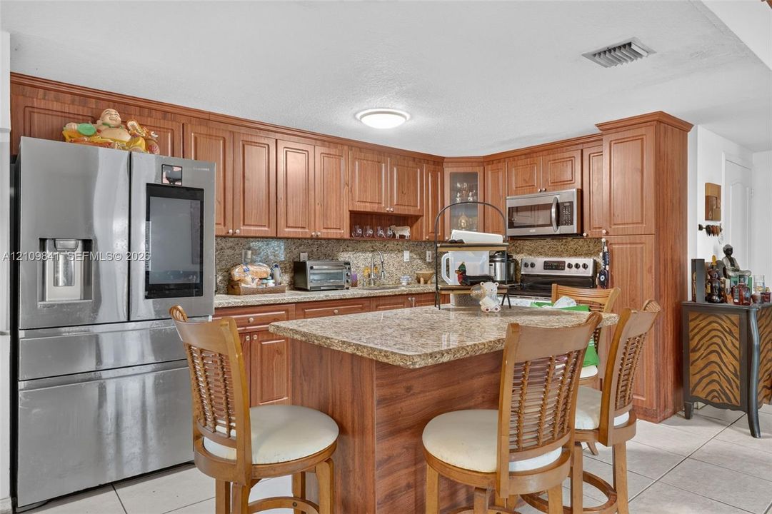 Kitchen featuring wood cabinetry, stone-finish countertops, stainless steel appliances, a center island, and tile flooring