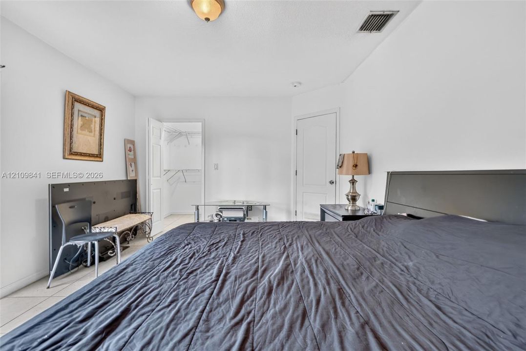 Neutral-toned room featuring tile flooring, a flush-mount ceiling light fixture, and a walk-in closet with built-in wire shelving