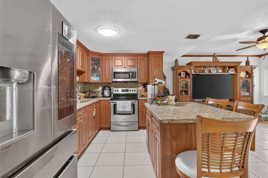 Kitchen featuring wood cabinetry, stone countertops, a center island with breakfast bar seating, stainless steel appliances, and tile flooring