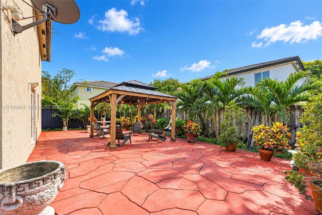 Rear patio featuring stamped concrete flooring, a covered wooden gazebo, and mature perimeter landscaping