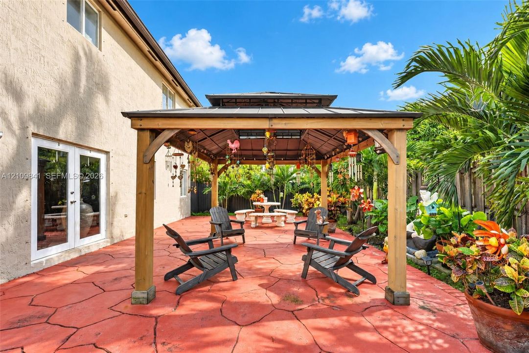 Backyard patio featuring a large wooden gazebo, stamped concrete flooring, and double glass doors