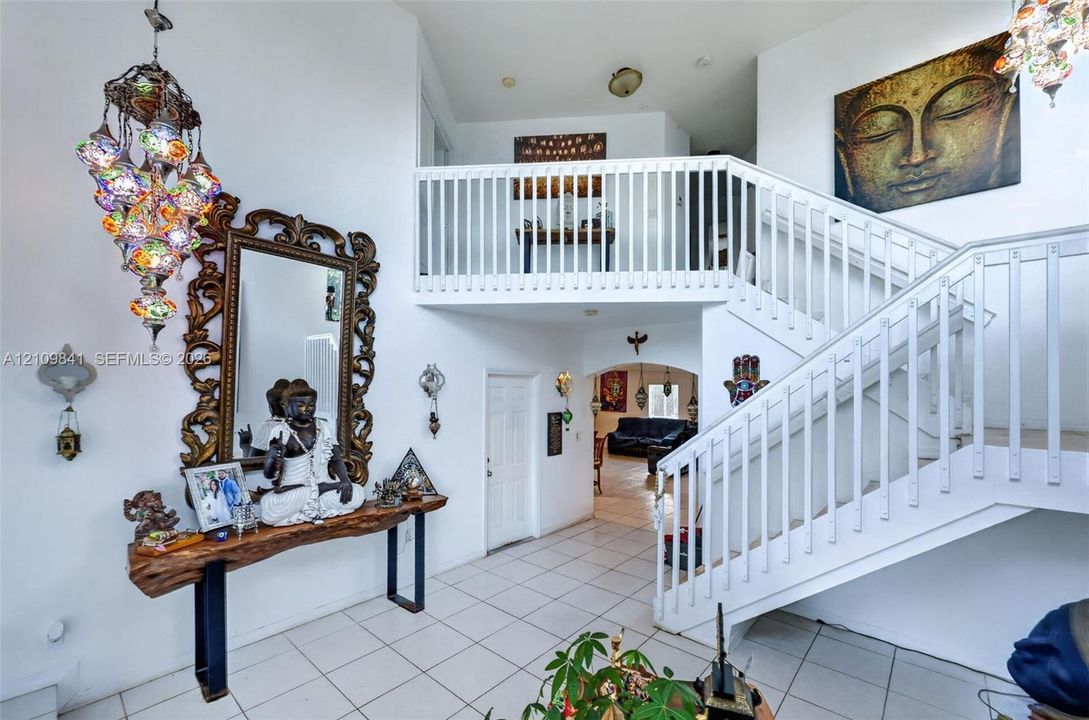 Entryway featuring double-height ceilings, a white wooden staircase with matching balusters, and neutral tile flooring