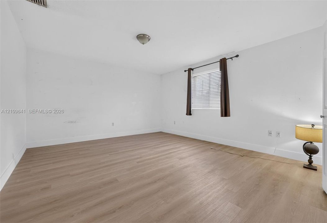 Interior space featuring wood-finish flooring, a neutral color palette, and a single-pane window with a horizontal blind