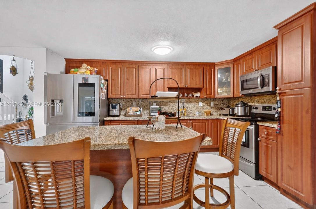 Kitchen featuring natural wood cabinetry, stone countertops, stainless steel appliances, a central island, and tile flooring