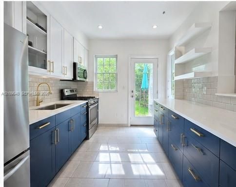 Kitchen featuring navy blue lower cabinetry, white upper cabinets, quartz countertops, subway tile backsplash, and metallic hardware
