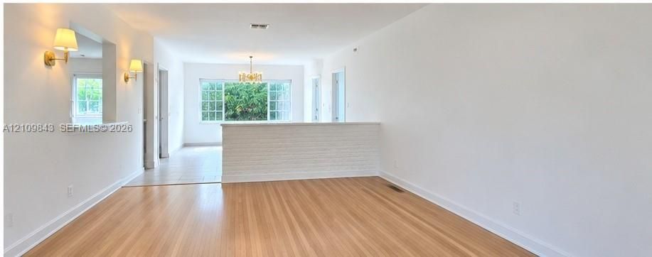 Open-concept interior featuring light wood-finish flooring, a white brick half-wall partition, wall-mounted light fixtures, and a multi-light chandelier