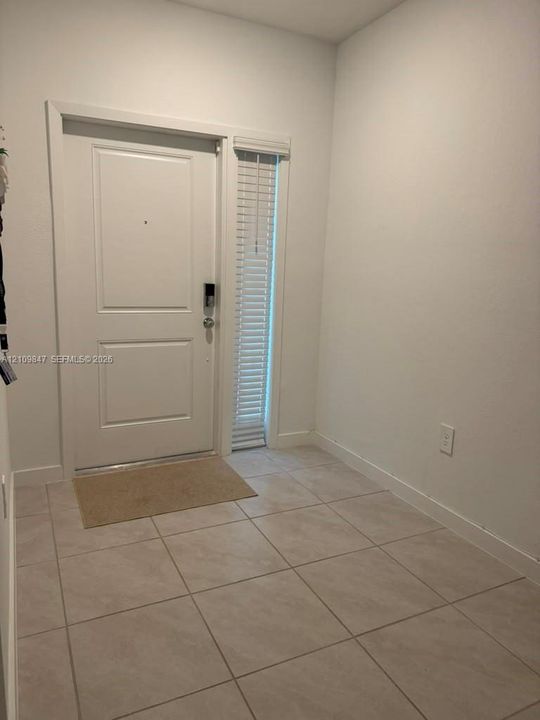 Entryway featuring neutral-toned floor tile, a paneled door with a metallic deadbolt, and a vertical side-light window with horizontal blinds
