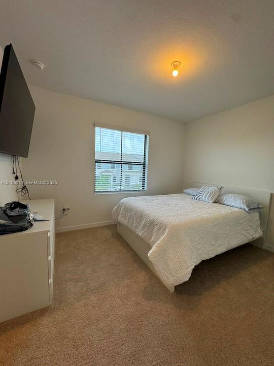 Bedroom featuring neutral-toned carpeting, off-white wall finishes, and a single-pane window with horizontal blinds