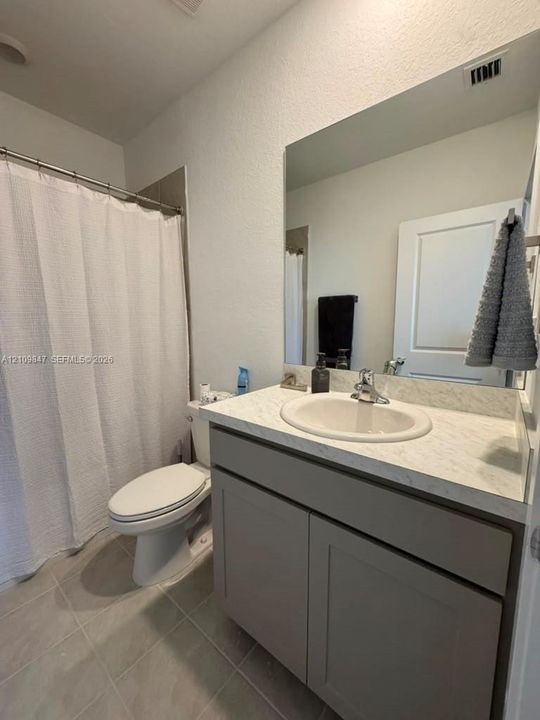 Bathroom featuring a vanity with shaker-style cabinetry, light-toned countertop, oval undermount sink, large wall-mounted mirror, and tile flooring