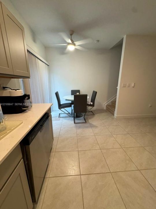 Kitchen featuring shaker-style cabinetry, stone-finish countertops, stainless steel dishwasher, tile flooring, and a ceiling fan