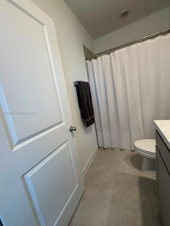 Bathroom featuring tile flooring, a two-panel interior door, vanity with a solid-surface countertop, and a shower with a curtain rod