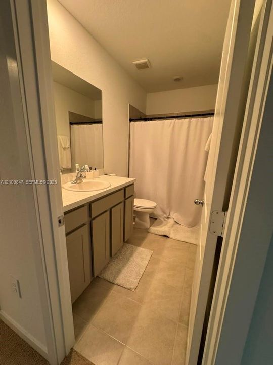 Bathroom featuring a vanity with neutral-toned cabinetry, solid surface countertop, integrated sink, and large wall-mounted mirror over ceramic tile flooring