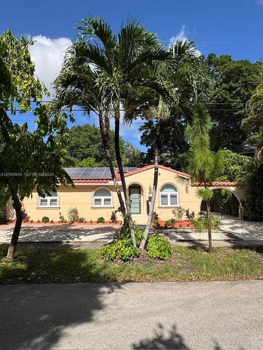 Stucco exterior featuring arched windows, a terracotta tile roof, integrated solar panels, and a decorative arched side entryway