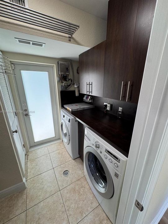 Laundry area featuring dark wood-finish cabinetry, a dark countertop, large-format tile flooring, and a glass-paneled exterior door