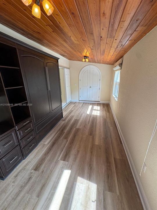 Vaulted wood-plank ceiling, integrated dark wood cabinetry with drawers, wide-plank wood-finish flooring, and arched double entry doors