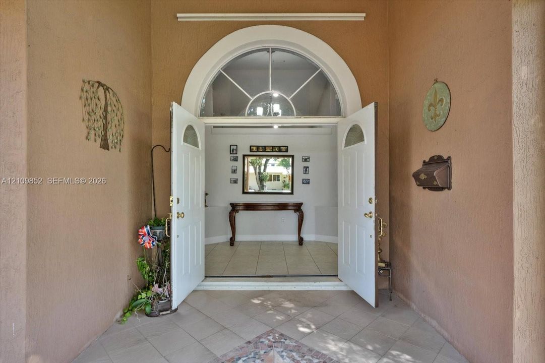 Covered entryway featuring a tiled porch and double doors with an arched fanlight window