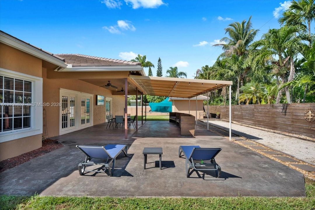 Expansive concrete patio featuring a covered outdoor living area, ceiling fans, and wood-paneled privacy fencing in the back and a concrete wall with lighting on the sides of the house and in the front *
