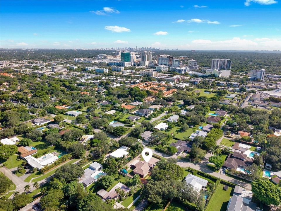 Aerial perspective showcasing this residential property situated within a mature landscape featuring extensive tree canopy and proximity to urban skyline of Downtown Dadeland *