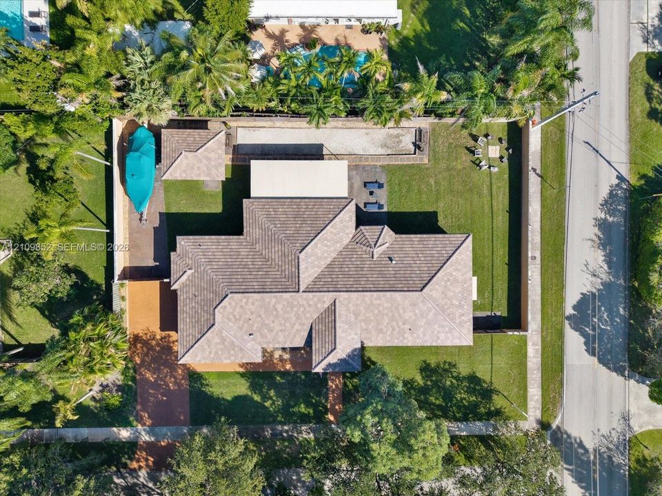 Aerial perspective featuring a multi-hipped roofline, expansive grass lawn, paved driveway, enclosed perimeter wall, and mature landscaping