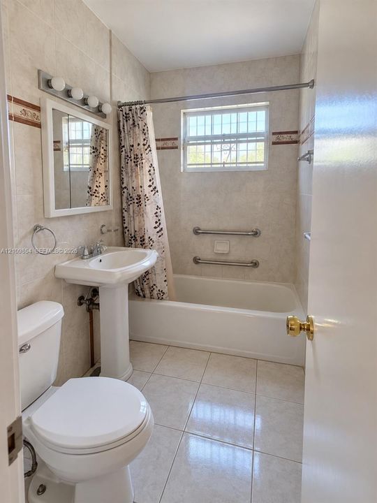 Full bathroom featuring neutral tile flooring, a pedestal sink, wall-mounted light fixture, and a shower-tub combination with stainless steel grab bars