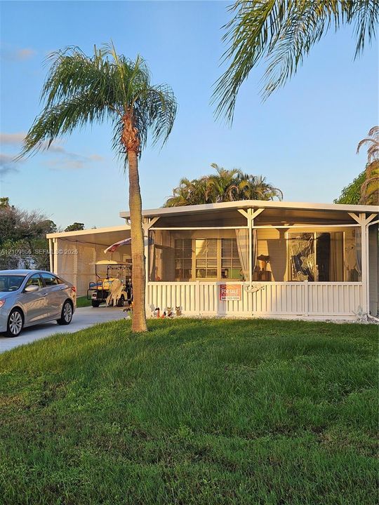 Single-story residence featuring a screened-in front porch, white vertical railing, a covered carport, and established palm trees