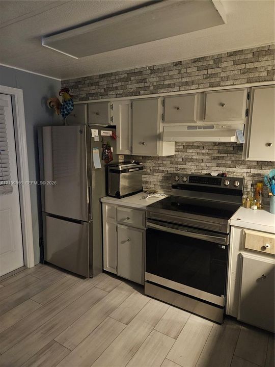 Kitchen featuring stainless steel refrigerator and range, custom cabinetry, tiled backsplash, and wood-finish flooring