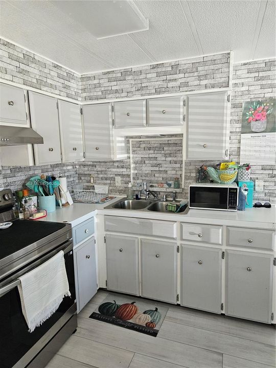 Kitchen featuring light grey cabinetry, a stainless steel dual-basin sink, a stainless steel range, and stone-finish wall surfacing