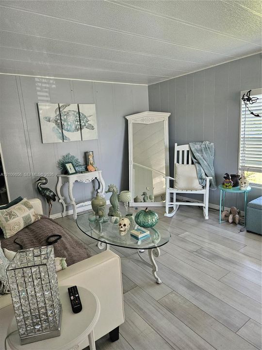 Light gray wood-finish flooring, panelled wall detailing, and horizontal window blinds