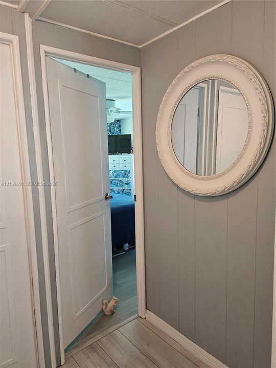 Gray paneled wall featuring a circular decorative mirror, wood-finish flooring, and a classic-style interior door