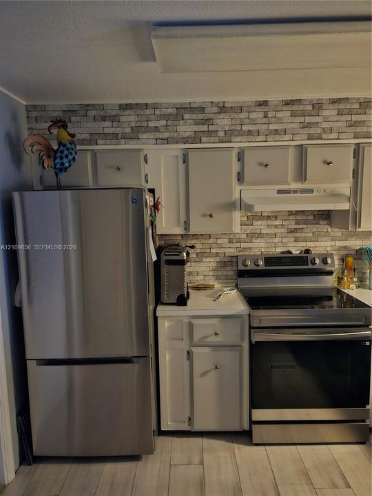Kitchen featuring stainless steel refrigerator and range, grey cabinetry, tile backsplash, and light-toned flooring