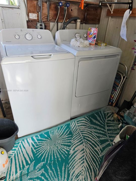 Laundry area featuring a top-load washer and a front-load dryer with exposed utility hookups and wall-mounted shelving