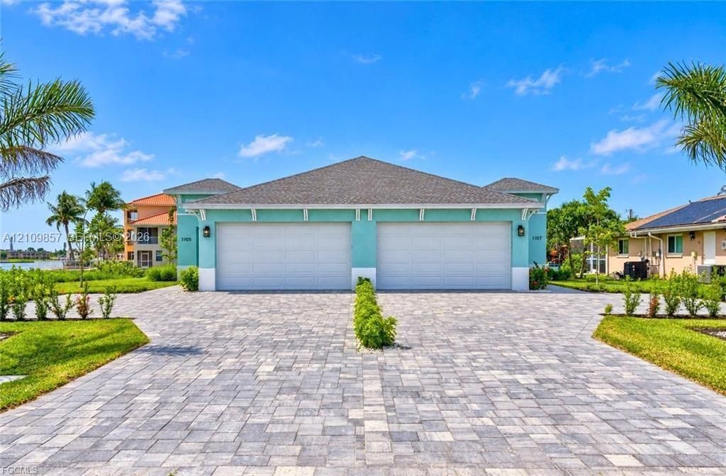 Exterior facade featuring dual garage doors, a stone-paver driveway, and professional landscaping