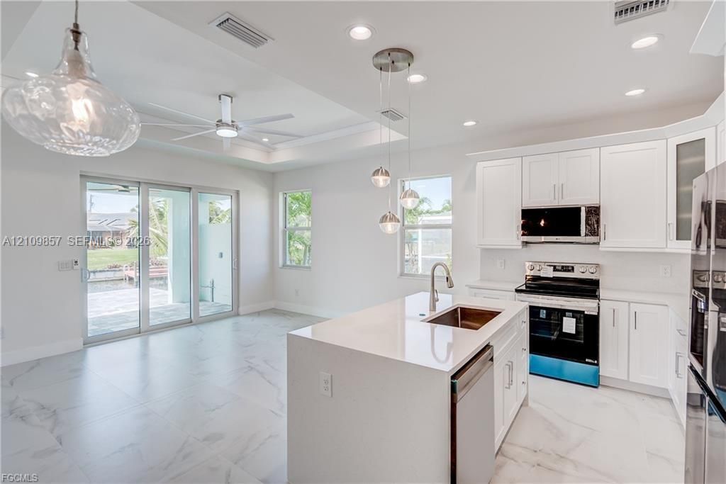 Kitchen featuring white shaker-style cabinetry, quartz countertops, a central island with a stainless steel undermount sink, recessed lighting, and large-format tile flooring
