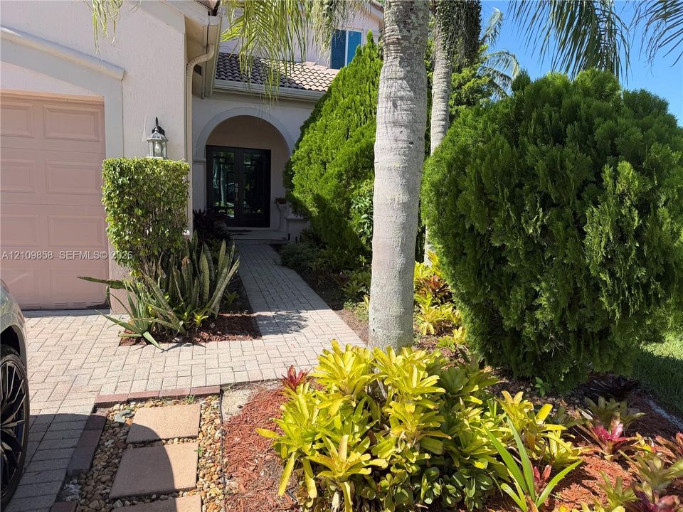Stucco exterior featuring an arched entryway, double-door entrance, paver walkway, and manicured landscaping