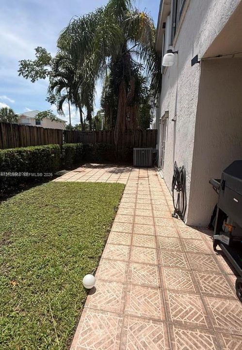 Outdoor area featuring a paved patio with patterned tiles, a manicured lawn, a privacy fence, and mature palm trees