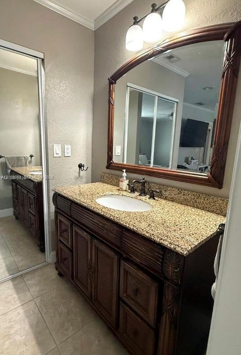 Dark wood vanity with a stone countertop, oval undermount sink, three-light fixture, and arched mirror, complemented by tiled flooring and a sliding mirrored closet door