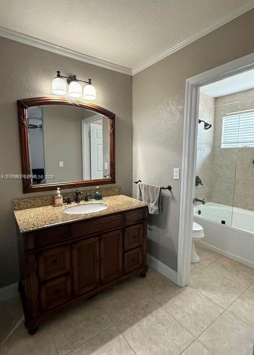 Bathroom featuring a dark wood vanity with stone-finish countertop, oval undermount sink, three-light fixture, arched wall mirror, and tile flooring with a separate bathing area