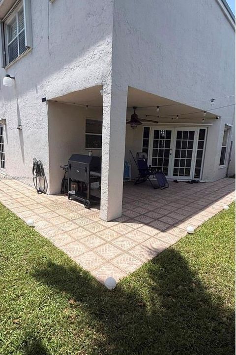 Covered patio featuring paver-style flooring, white exterior stucco walls, a ceiling-mounted fan, and glass-paneled French doors