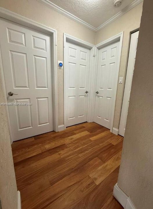 Hallway featuring wood-finish flooring, six-panel interior doors, and crown molding
