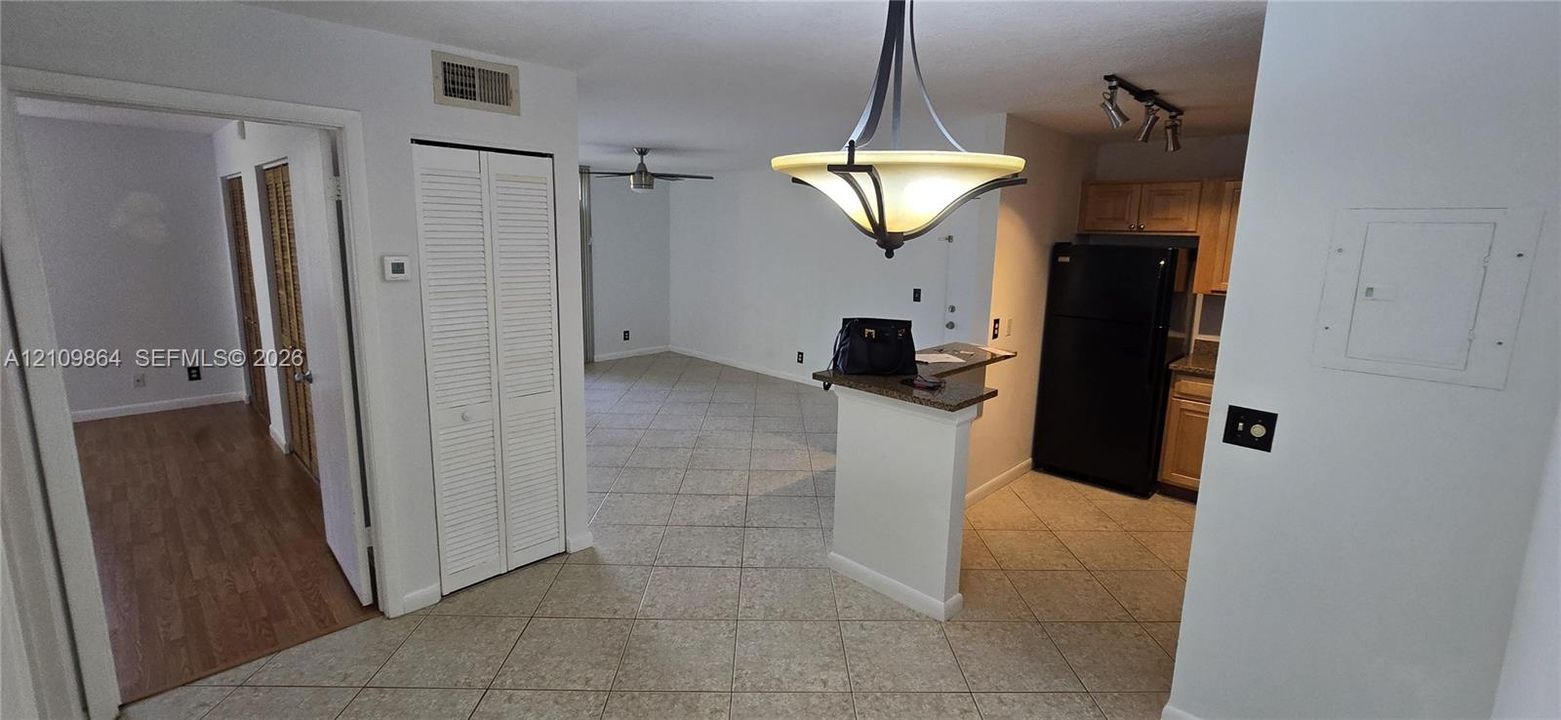 Interior space featuring tile flooring, wood-finish flooring, a kitchen breakfast bar with stone-finish countertop, bi-fold closet doors, and decorative pendant lighting
