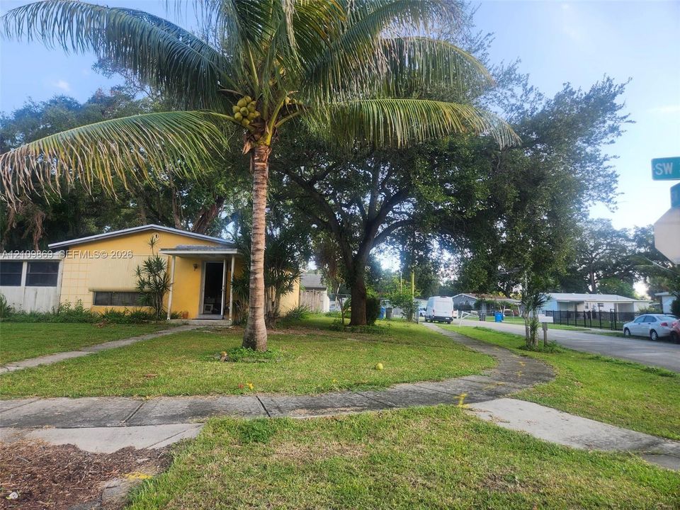 Single-story exterior featuring a concrete block facade, covered entryway, and mature palm tree on a corner lot
