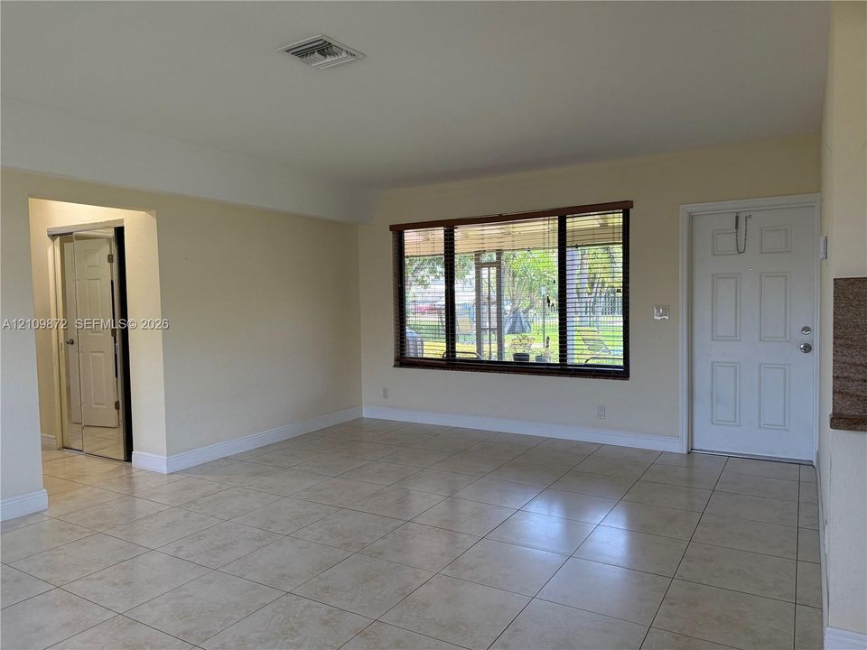 Neutral-toned ceramic tile flooring, expansive window with dark trim, multi-panel exterior entry door, and a built-in mirrored closet door