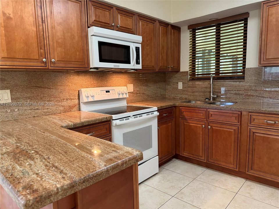 Kitchen featuring wood cabinetry, stone countertops with integrated backsplash, white electric range with over-the-range microwave, and tile flooring