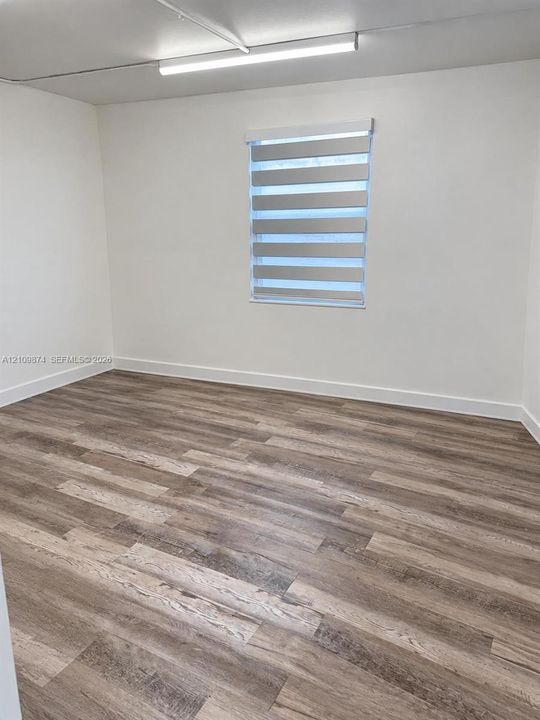 Neutral interior featuring wood-finish flooring, white walls, a dual-layer roller shade, and ceiling-mounted linear lighting