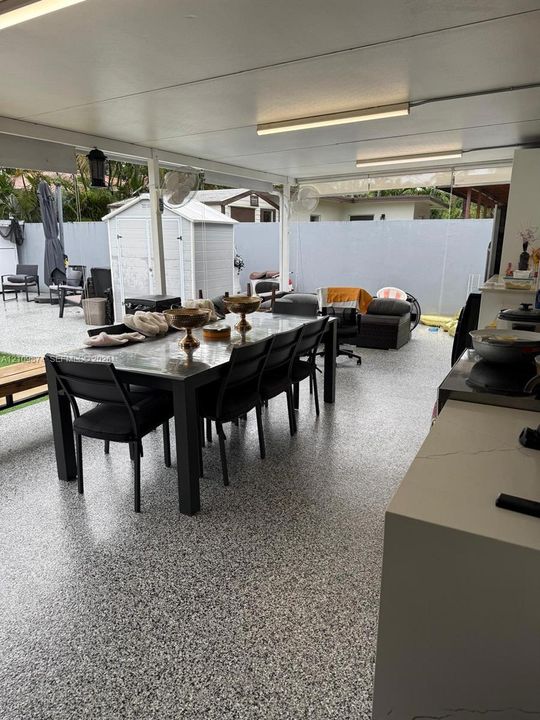 Covered outdoor patio featuring a speckled epoxy floor coating, built-in countertop, overhead fluorescent lighting, and mounted wall fans