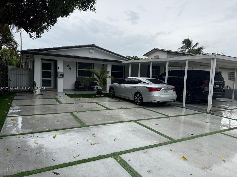 Exterior featuring a paver driveway with turf accents, a covered carport, and a white privacy gate