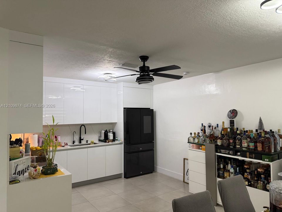 Kitchen featuring high-gloss white cabinetry, light-toned tile flooring, a dark-finish faucet, and a black ceiling fan with integrated lighting