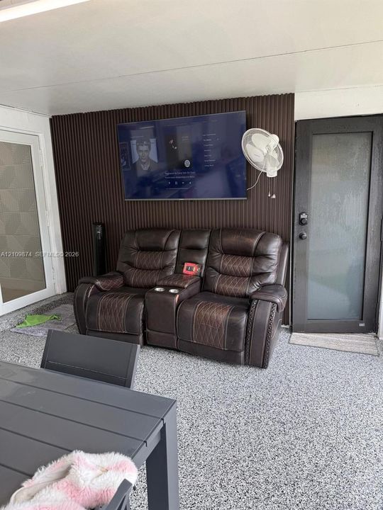 Covered outdoor area featuring textured vertical slat wall paneling, speckled epoxy flooring, and a glass-paneled exterior door